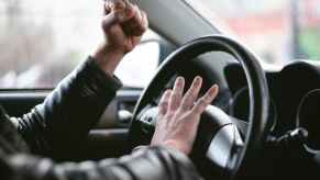 A man wearing a leather jacket honking a car's horn