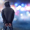 A man in hand cuffs in front of police cars