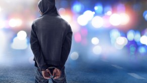 A man in hand cuffs in front of police cars