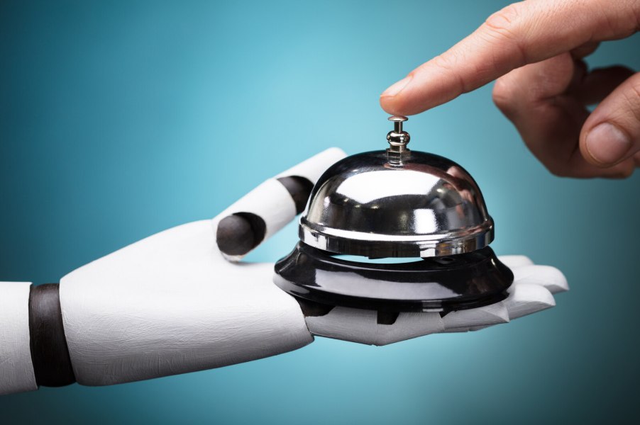 Robot hand holds a service bell while human hand presses bell top