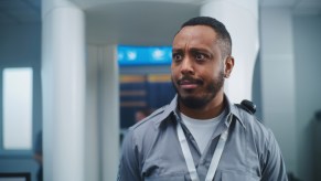 Male TSA staff member makes an uncomfortable expression with body scan machine in background