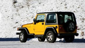 A yellow Jeep Wrangler parked by a snowy bank